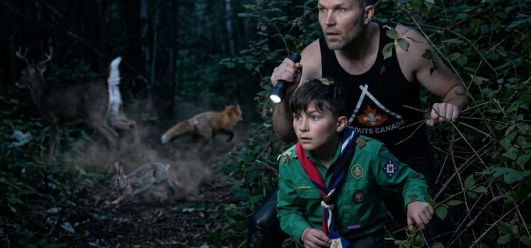 Sébastien et son fils Alexandre en uniforme scout explorant la forêt la nuit avec une lampe de poche au milieu d'animaux sauvages.